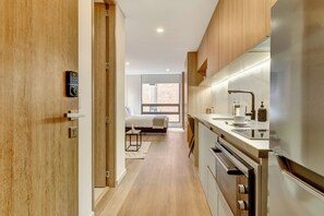 Eine moderne Küche mit Edelstahlgeräten, einer Holztür und Blick auf ein Schlafzimmer mit Bett und Fenster.