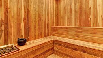 A sauna with wooden walls and benches, a black container with a wooden spoon, and a tray with stones.