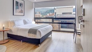 A modern bedroom with a large window, a bed, a bedside table with a lamp, and a framed picture on the wall. - Haus by Wynwood House (Bogotá)