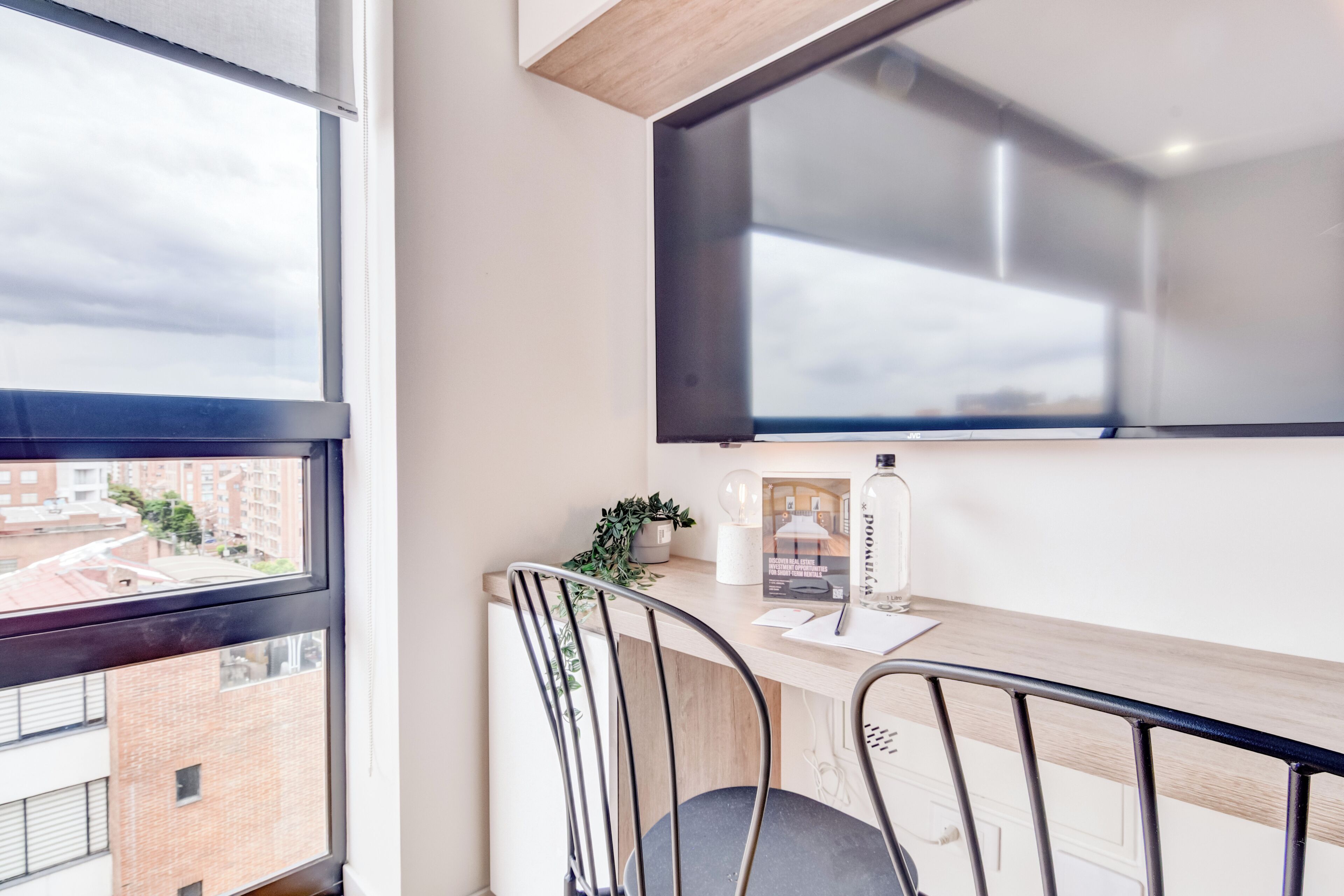 A modern workspace with a desk, two chairs, a window, and a view of buildings.