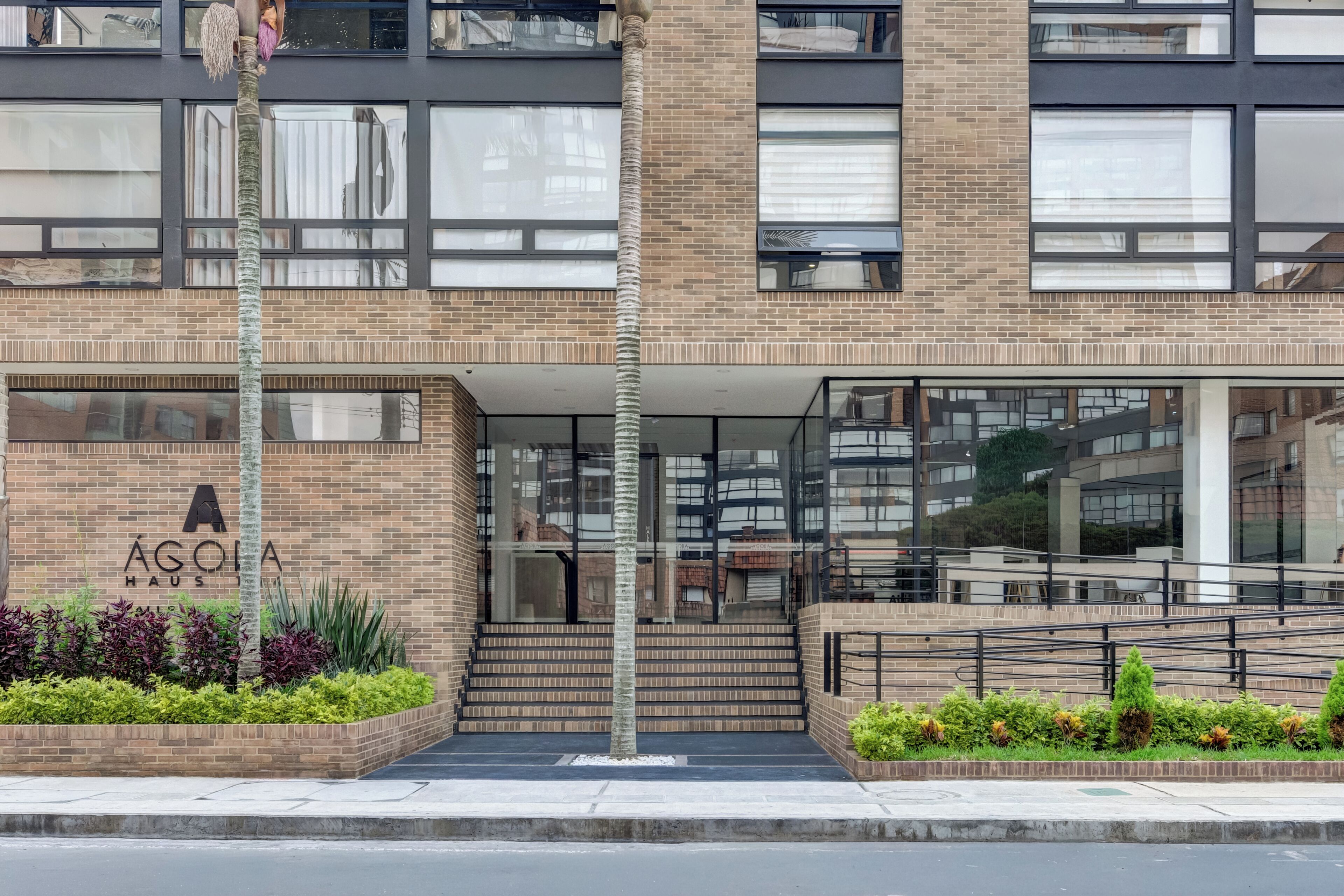 Un edificio moderno con facciata in mattoni, un cartello con su scritto 'AGOLIA HAU' e una scalinata che conduce all'ingresso.