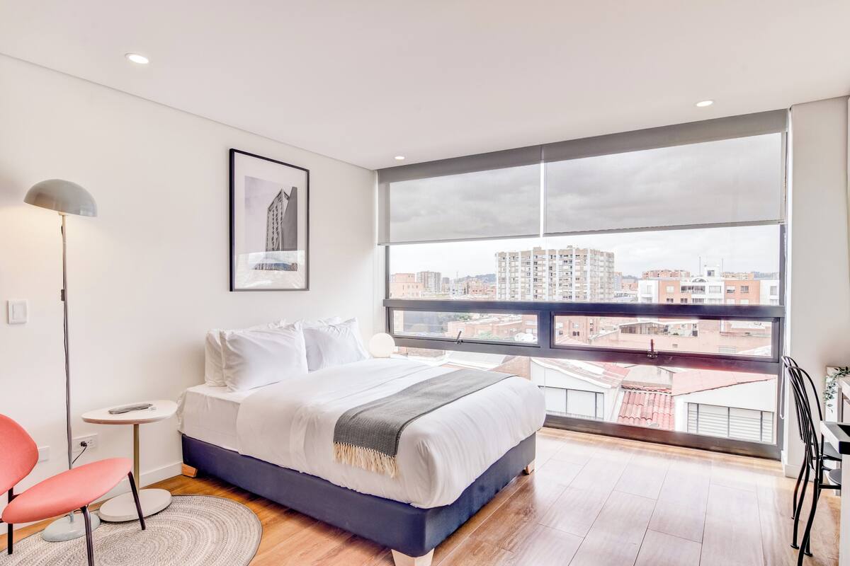 A modern bedroom with a large window, a bed, a chair, and a small table.