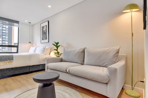 Ein modernes Wohnzimmer mit einer Couch, einem runden Couchtisch, einer Stehlampe und einer Zimmerpflanze.
