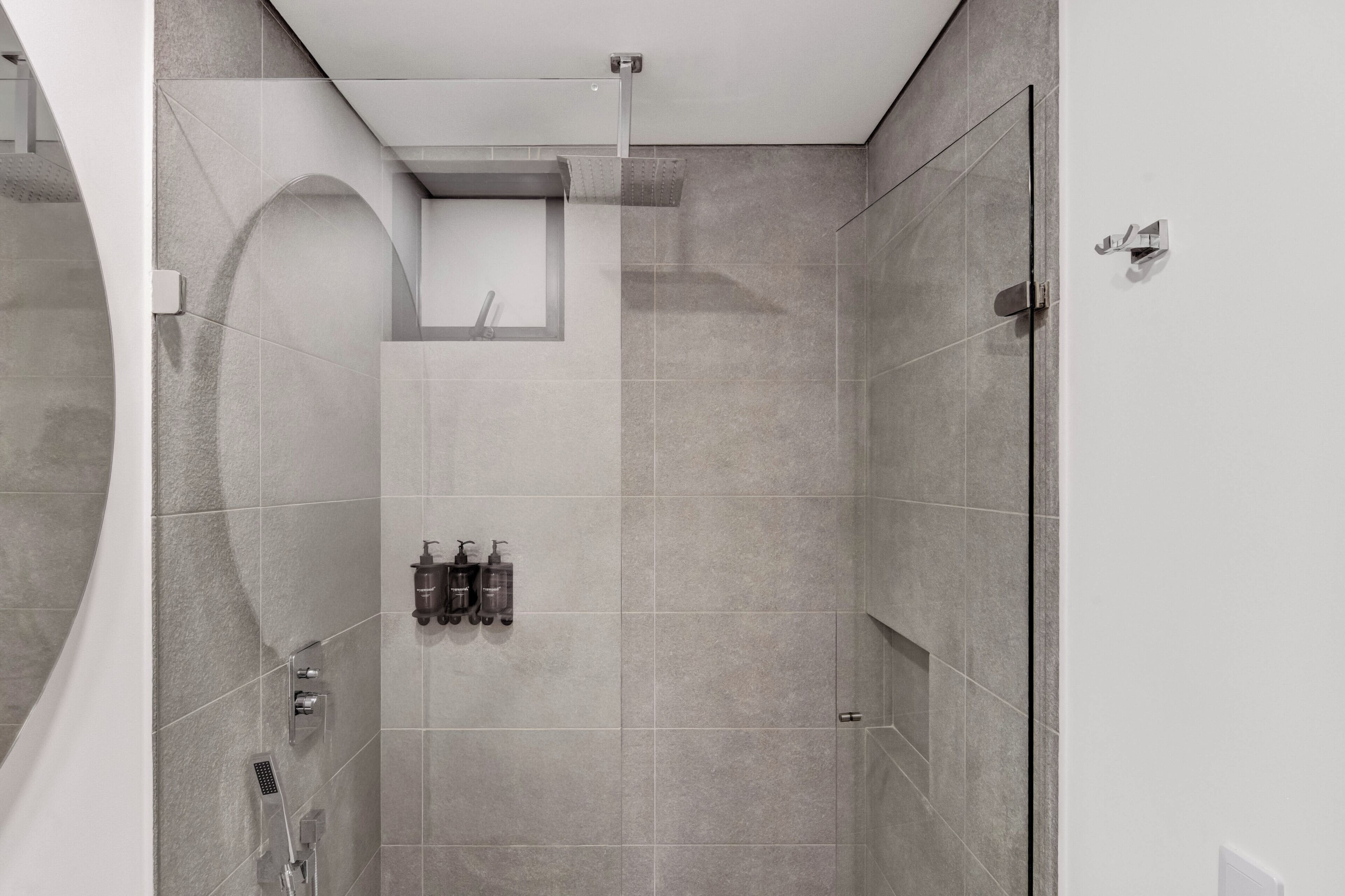 Un área de ducha moderna con puerta de cristal, estante empotrado con artículos de aseo y ducha montada en la pared.