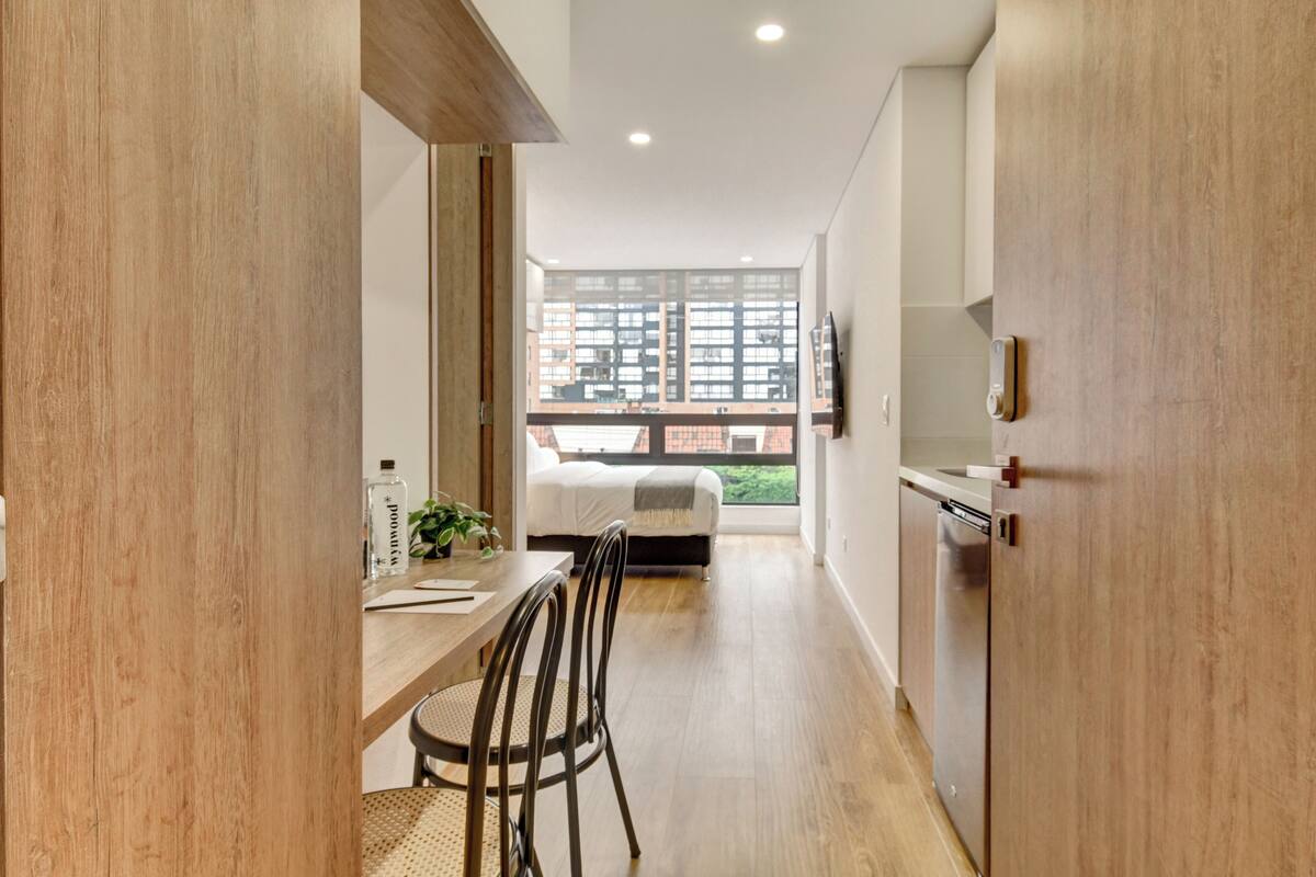 A modern interior with a dining area, a bed, and a view of buildings through large windows.