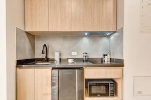 A compact kitchen with wooden cabinets, a stainless steel sink, a dishwasher, and a microwave.