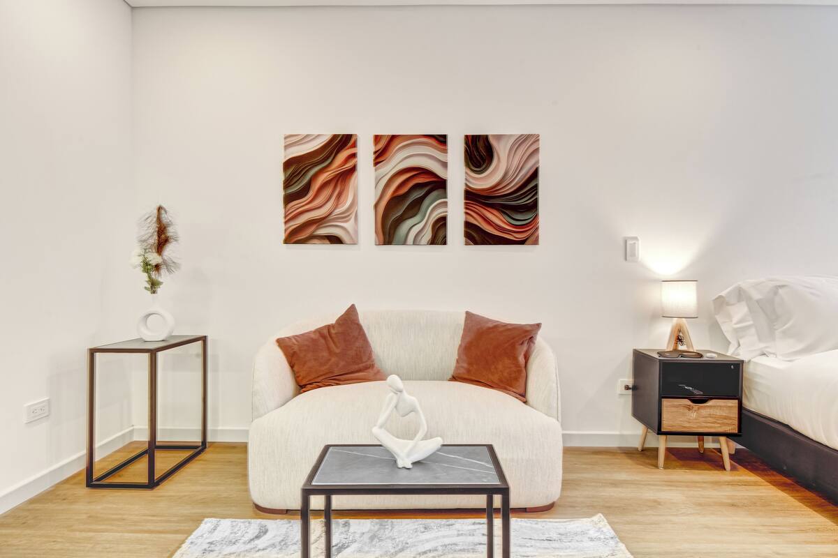A modern bedroom with a sofa, a small table, a nightstand, and abstract wall art.