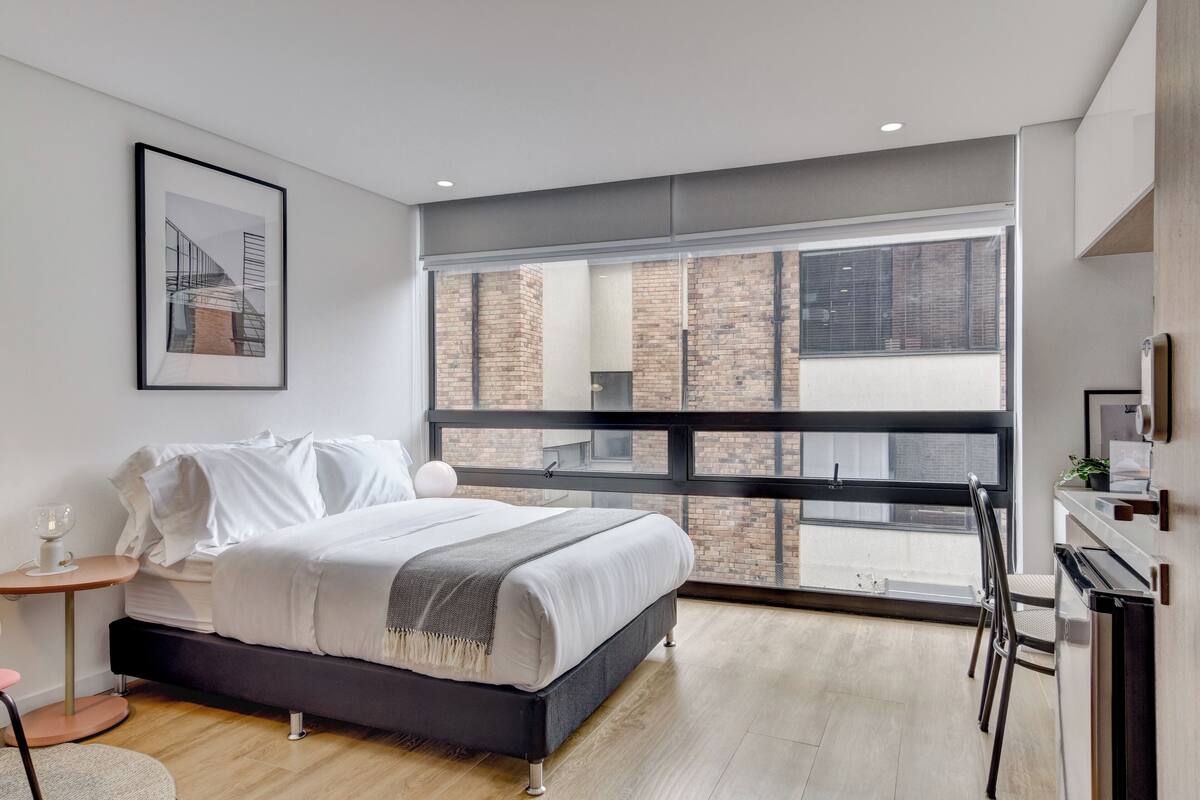 A modern bedroom with a large window, a bed, a bedside table, and a chair.