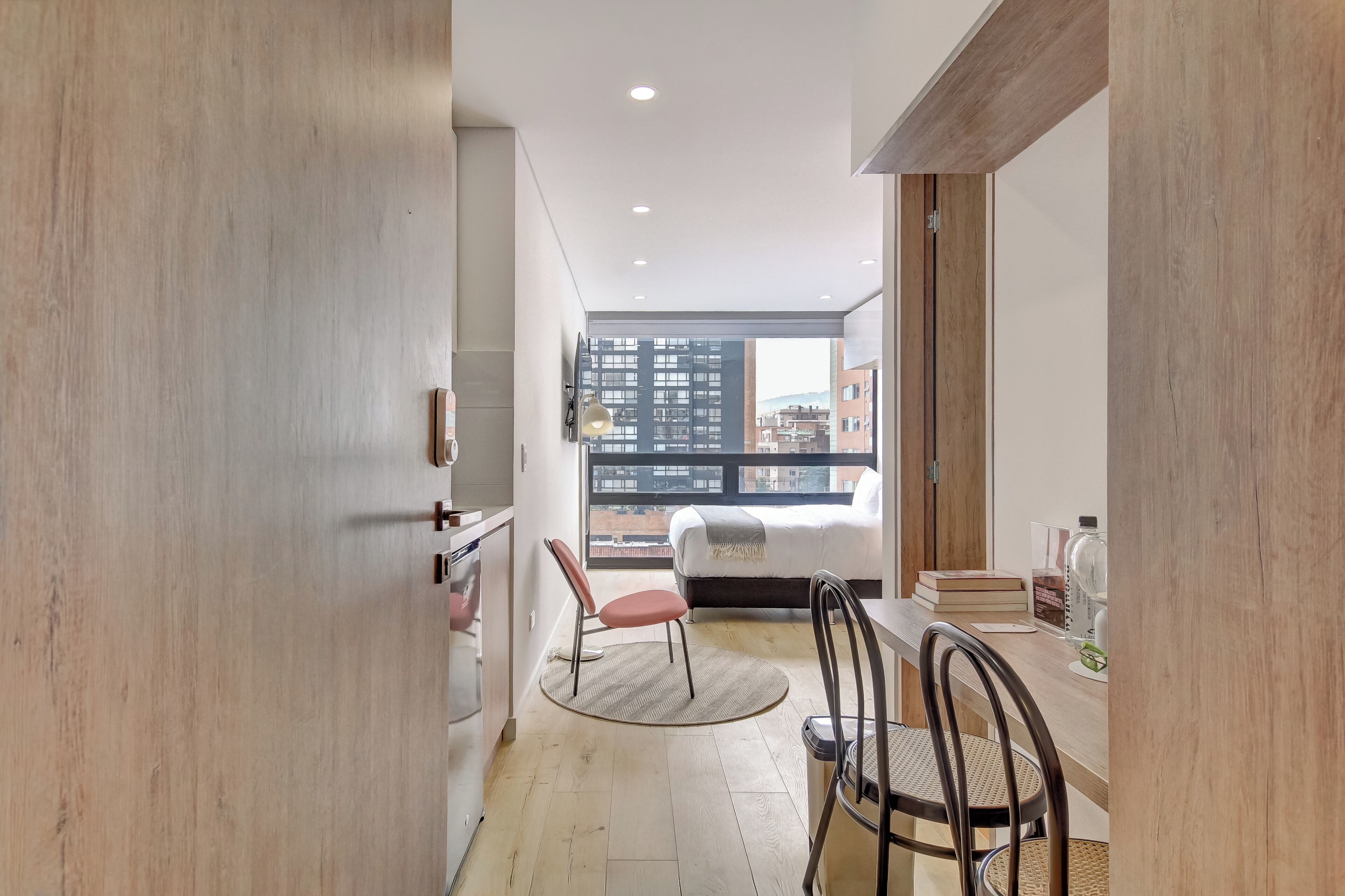 A modern apartment with a kitchen, dining area, and a bedroom with a city view.
