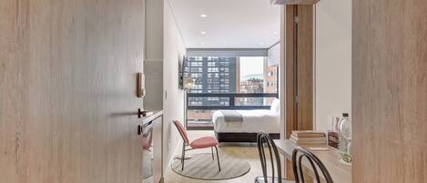 A modern apartment with a kitchen, dining area, and a bedroom with a city view.