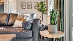 Een moderne woonkamer met een leren bank, een ronde houten tafel en een potplant.