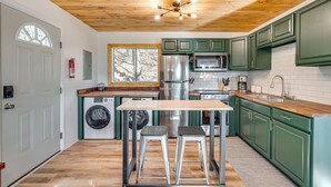 Een compacte keuken met houten plafond, groene kasten, roestvrijstalen apparatuur en een centraal eiland met krukken.