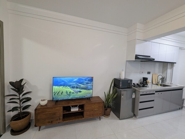 A modern kitchen with a built-in microwave, a refrigerator, and a wooden cabinet below a flat-screen TV. - Tranquil Apartment in Vibrant Westlands (Nairobi)