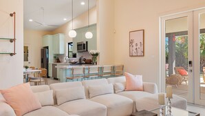 A modern living room with a sectional sofa, a glass coffee table, and a view of the kitchen and dining area.
