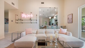 A modern living room with a sectional sofa, a glass coffee table, and a neon sign on the wall.