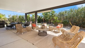 An outdoor patio area with wicker furniture, a round table, and a view of tropical vegetation.