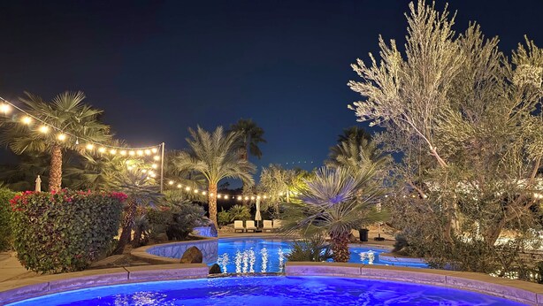 A nighttime pool area with string lights, palm trees, and a clear blue pool.