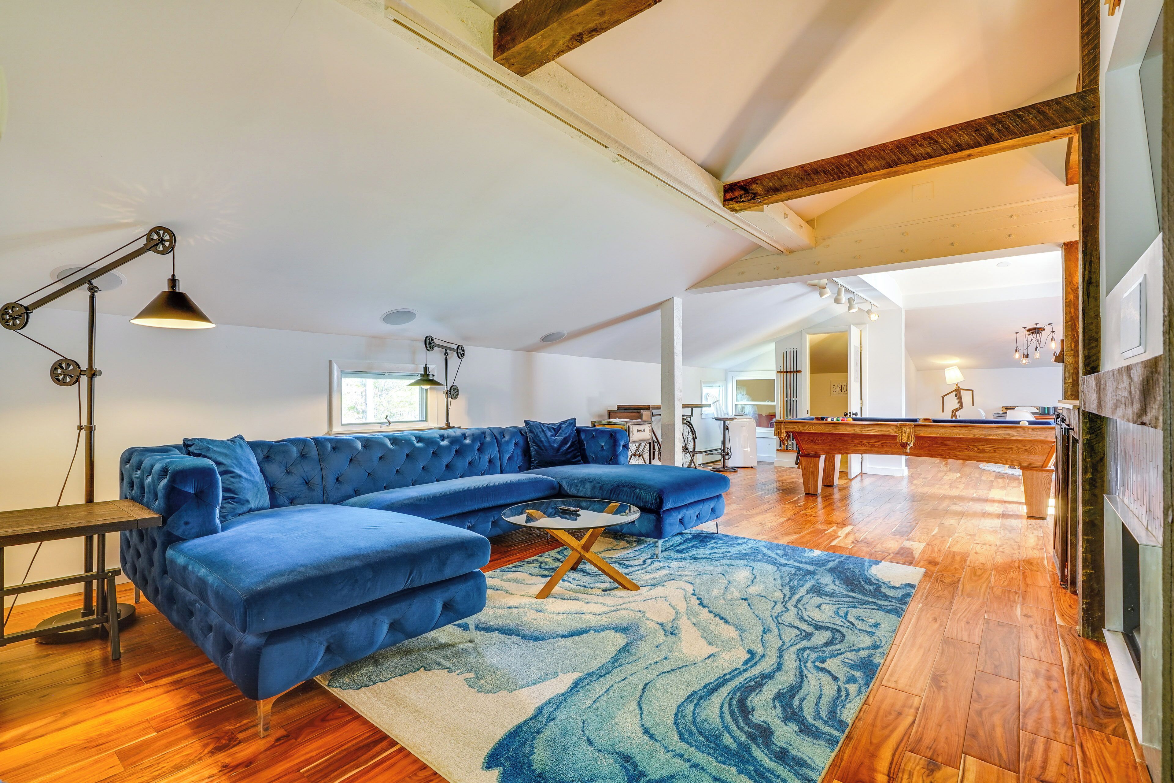 A spacious living room with a blue sectional sofa, wooden flooring, and a large rug.