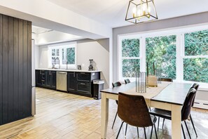 A modern kitchen with dark cabinetry, a wooden floor, and a dining area with a table and chairs. - 2 Mi to USCG Academy! Convenient New London Home (New London)