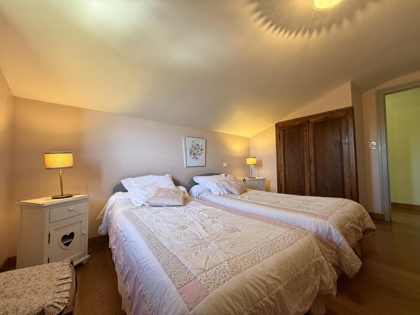 Ein Schlafzimmer mit zwei Betten, einem Nachttisch mit herzförmiger Schublade, einem kleinen Tisch und einem Holzschrank.