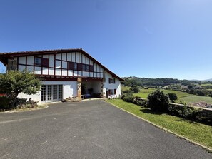 A two-story building with a large driveway and a view of rolling hills. - ANIOTZ-BEHEREA - SARE (SARE)