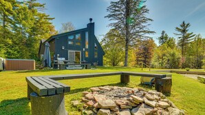Ett modernt hus med en eldstad av sten på gården, omgivet av träd och ett picknickbord.