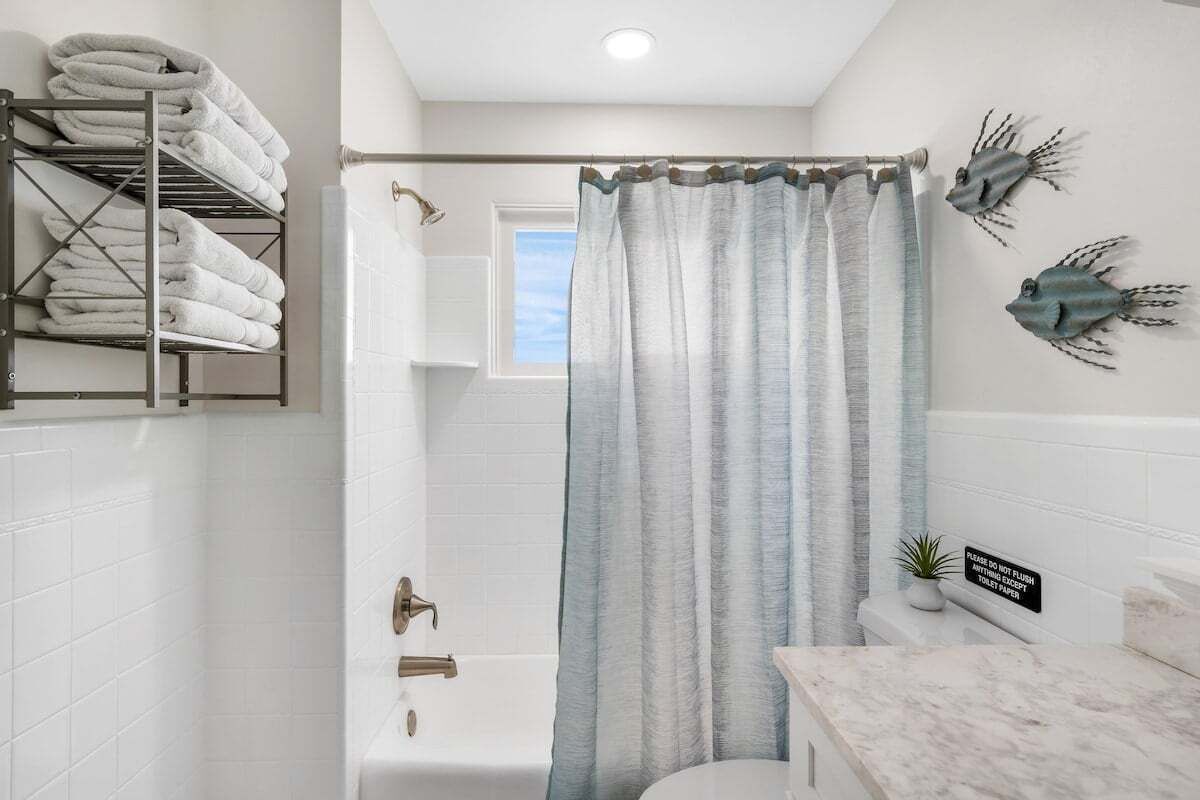 A bathroom with a shower curtain, a towel rack, a toilet, and a sign on the wall.
