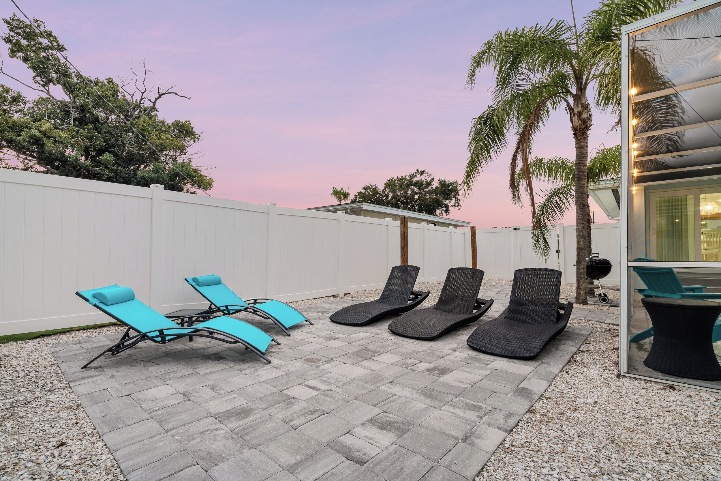 A patio with four lounge chairs, a barbecue grill, and a glass enclosure.