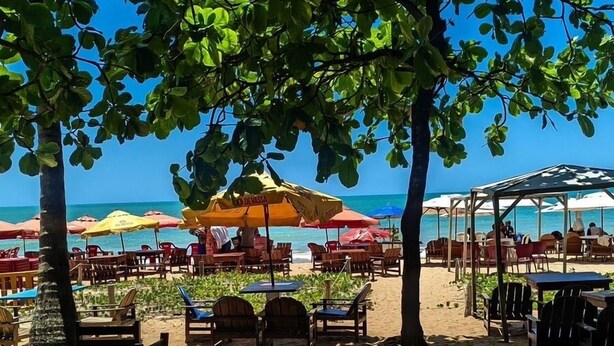 Un café situé en bord de mer, avec une terrasse et des parasols, offrant une vue sur l’océan.