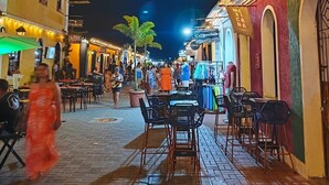Une scène de rue nocturne avec des terrasses, des bâtiments illuminés et un mélange de piétons.