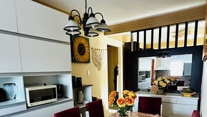 Un comedor con una mesa redonda, sillas tapizadas en rojo, un mantel estampado y una lámpara colgante.