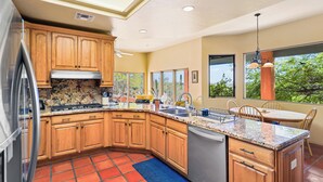 A kitchen with wooden cabinets, granite countertops, a dishwasher, and a dining area with a table and chairs. - Sonoran Retreat w/ Hot Tub near Starr Pass Golf & Saguaro Park (Tucson)