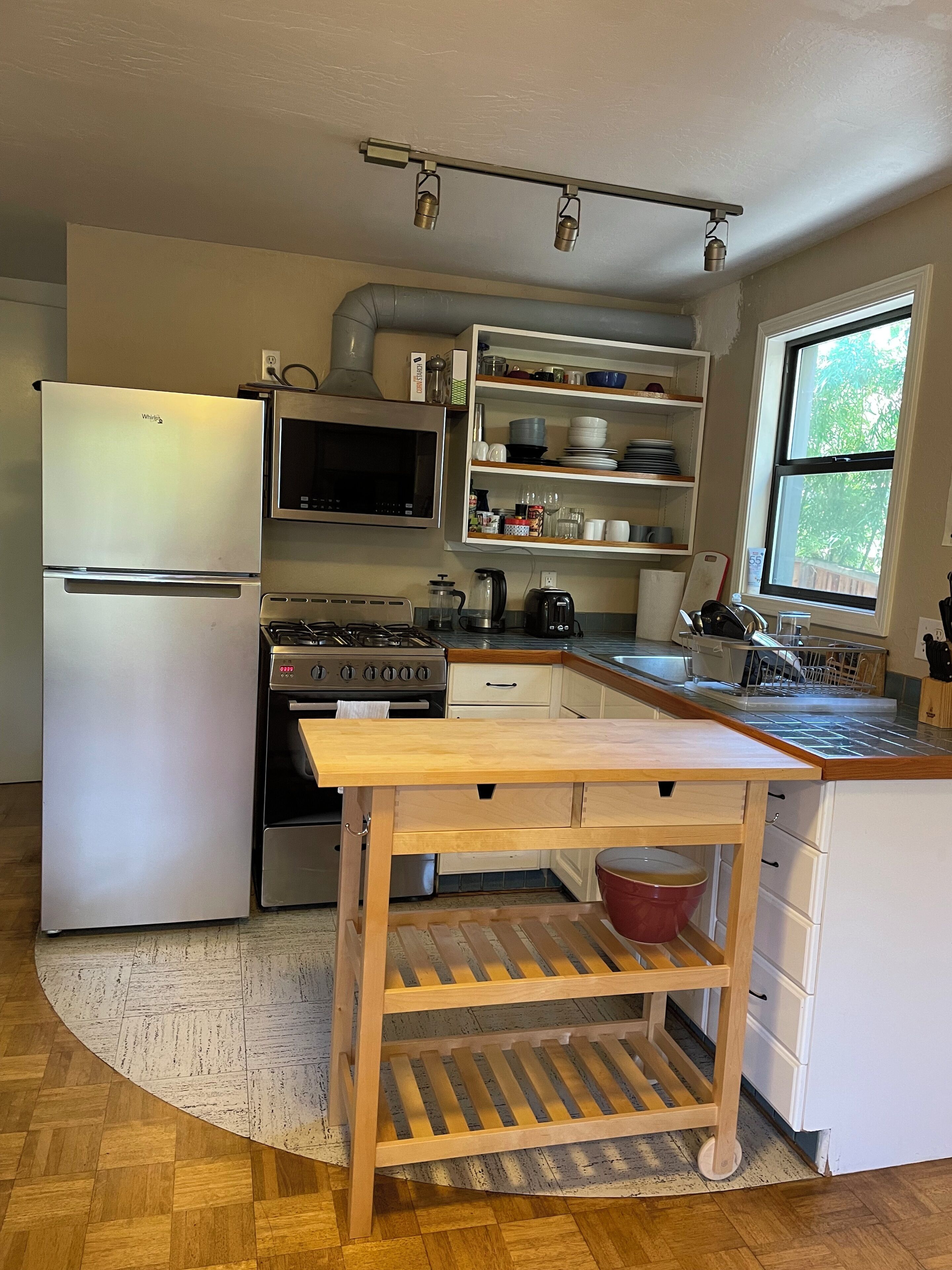A compact kitchen with a refrigerator, stove, microwave, and wooden island with a sink.