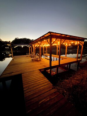 Ein hölzerner Pavillon mit Lichterketten, eine Holzterrasse und ein ruhiger See im Abenddämmerung.