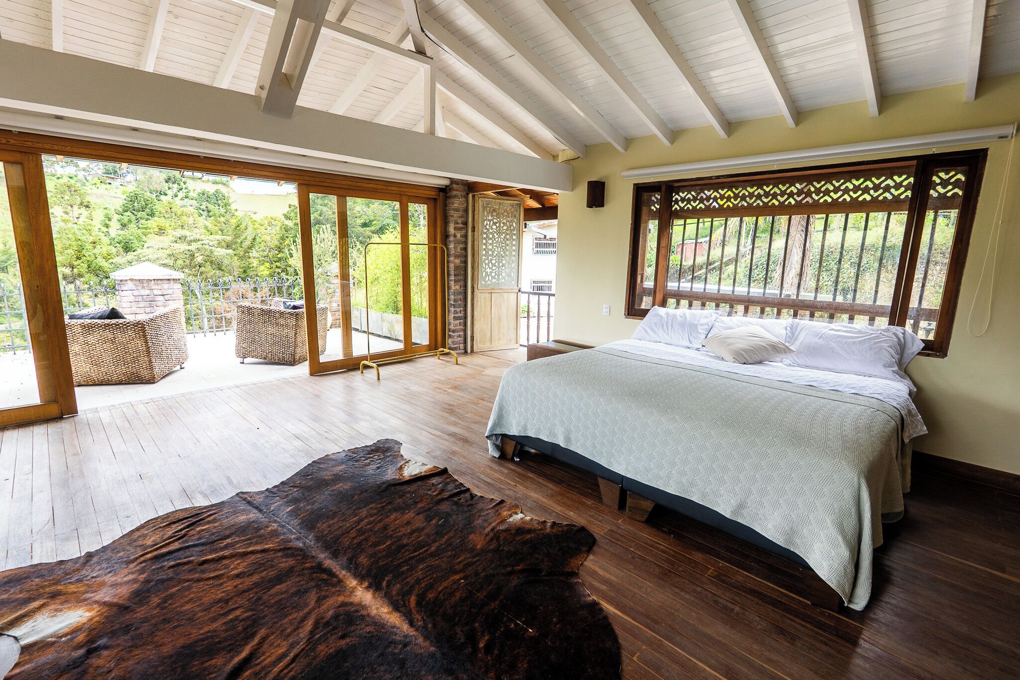A spacious bedroom with a large bed, wooden flooring, and a view of the outdoors through large sliding doors.