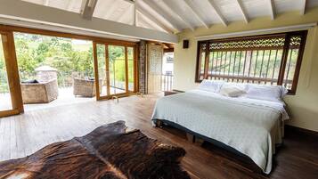 A spacious bedroom with a large bed, wooden flooring, and a view of the outdoors through large sliding doors.