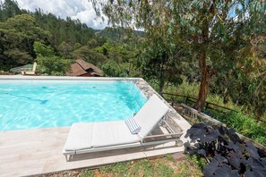 A clear swimming pool with lounge chairs and a view of a forested area. - Sahara Lodge: Nature, Design & Arabian Horses (El retiro)
