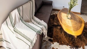 A modern living room with a brown sofa, a woven mirror, a wooden coffee table, and a cowhide rug. - Sahara Lodge: Nature, Design & Arabian Horses (El retiro)