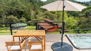 Eine Holzterrasse mit Tisch, Stühlen, einem Whirlpool und einem großen Sonnenschirm.