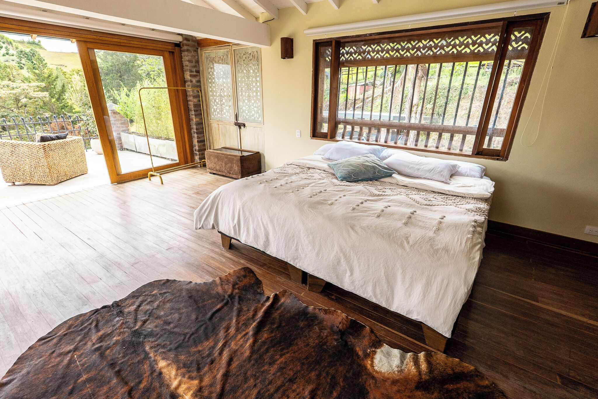Ein Schlafzimmer mit einem großen Bett, Holzboden, Blick durch eine Schiebetür und einem großen Teppich.