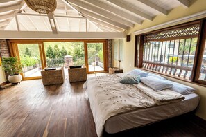 A bedroom with a large bed, wooden flooring, a balcony with a view of greenery, and a large window with a decorative screen. - Sahara Lodge: Nature, Design & Arabian Horses (El retiro)