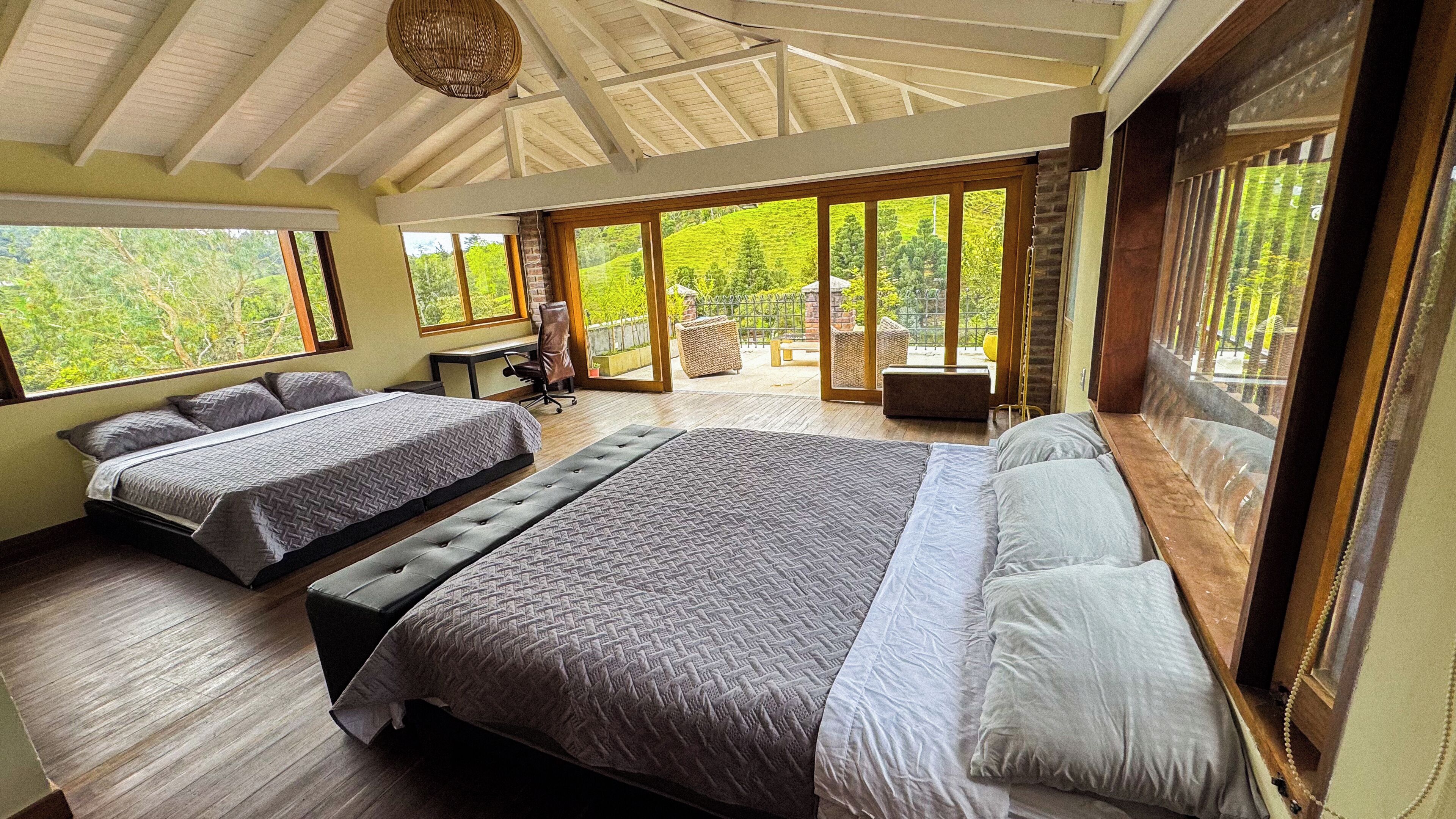 A bedroom with two beds, a desk, and a view of the outdoors.