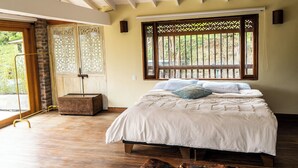 A bedroom with a bed, a window with bars, a wooden floor, and a door with a decorative screen. - Sahara Lodge: Nature, Design & Arabian Horses (El retiro)