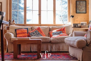 A cozy living room with a large window, a wooden coffee table, and a patterned rug. - Discover this charming ground floor apartment, located in the peaceful region of Médran. Carefully r (Verbier)