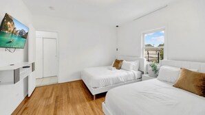 A bedroom with two beds, a TV mounted on the wall, and a window with a view of the outdoors. - Spacious 3BR Luxe Escape near NYC (Yonkers)