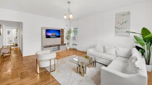 A modern living room with a flat-screen TV, white sofas, a glass coffee table, and a wooden floor. - Spacious 3BR Luxe Escape near NYC (Yonkers)