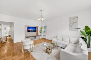 Una sala de estar moderna con televisor de pantalla plana, sofás blancos, una mesa de centro de vidrio y suelo de madera.