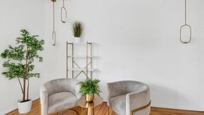 A modern living room with two grey armchairs, a round wooden coffee table, a white shelving unit, and two potted plants. - Spacious 3BR Luxe Escape near NYC (Yonkers)