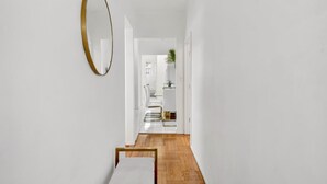A narrow hallway with a wooden floor, a white wall, and a gold-framed mirror. - Spacious 3BR Luxe Escape near NYC (Yonkers)