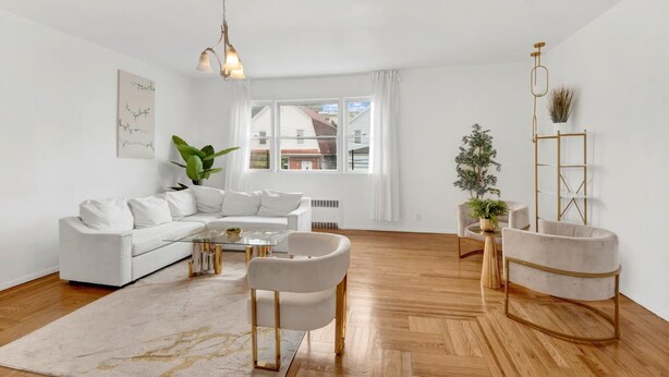 A modern living room with a white sofa, a glass coffee table, and a round armchair. There is a wooden floor and a large window with curtains. - Spacious 3BR Luxe Escape near NYC (Yonkers)